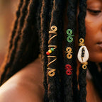 Gros plan sur des Locks ornées de bijoux en fil doré, cauris et perles, portés par une femme